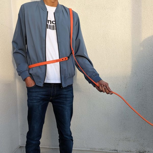 Man wearing the Dog A La Mode hands free and double ended orange vegan dog lead across the body and shoulder outdoors